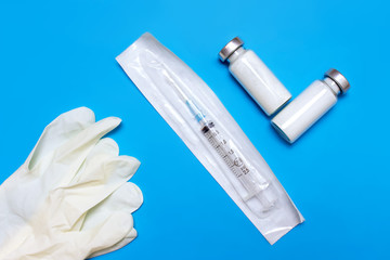 Wall Mural - Medical gloves, packed syringe and vials on blue background, flat lay, top view