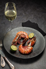 Two jumbo shrimps with lime for dinner on dark plate and glass of vine. Food background. Top view. Vertical composition.