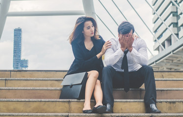 Business man is feeling sadness has problems life crisis about work sitting on the stairs in the city and businesswoman his colleagues tried to reassure his