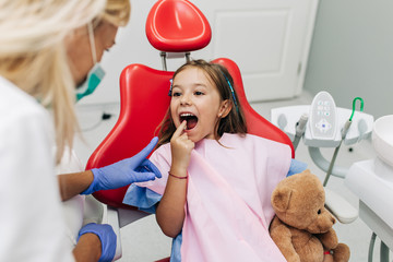 Cute little girl sitting on dental chair and having dental treatment.