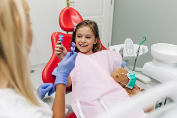 Wall Mural - Cute little girl sitting on dental chair and having dental treatment.