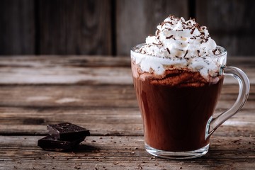 Hot chocolate drink with whipped cream in a glass on a wooden background