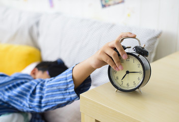 Asian boy sleepy and turn off alarm clock falls out of bed