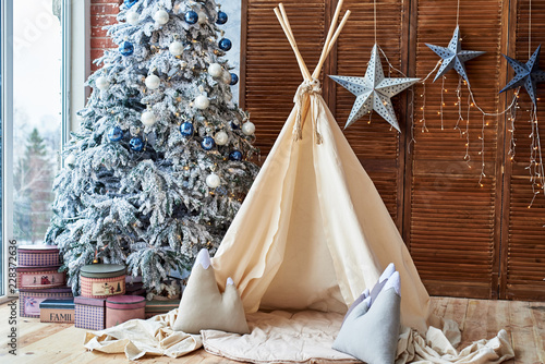 Fotografía Christmas tree with gifts and wigwam near window in child room, copy space