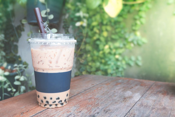 Iced coffee bubble with plastic takeaway glass on the wood table at the garden