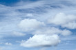 Group of puffy cumulus clouds with thin cirrus clouds behind them; blue sky.