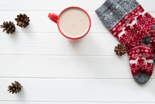 Hot Cacao In Red Cup On White Wooden Table Background, Red Socks With Christmas Ornament And Fir (pine) Cones.