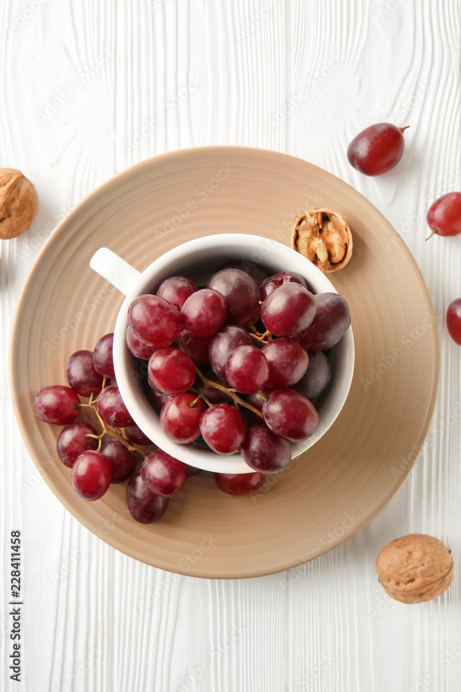Cup with sweet grapes on white wooden table