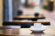 A small espresso coffee cup on a round wooden table outdoors.