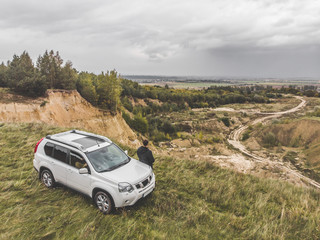 white suv at the top of the hill in autumn overcast weather. man standing near car around wild nature