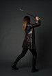 © faestock - full length portrait of brunette girl wearing long leather coat and boots. standing pose and holding a sword on grey studio background.