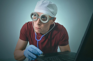 Computer technician engineer in the medical gloves and with stethoscope is repairing a laptop computer.