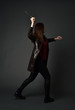 © faestock - full length portrait of brunette girl wearing long leather coat and boots. standing pose and holding a sword on grey studio background.