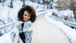 © Dirima - Cheerful stylish afro hair woman portrait under the snow at winter mountain road. Female wearing warm clothes and gloves.