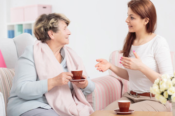 Wall Mural - Young woman talking with grandmother drinking tea during meeting