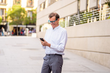 Smiling attractive stylish mature man using smart phone in urban outdoors city