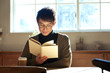 © amanaimages - 部屋で読書をする20代男性