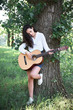 © soleg - young woman walking in the forest and playing guitar, summer nature, bright sunlight, shadows and green leaves, romantic feelings