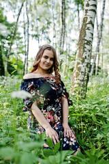 Portrait of a fabulous young girl in pretty dress with stylish curly hairstyle posing in the forest or park.