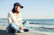 © amanaimages - Young woman sitting on retaining wall and looking at sea