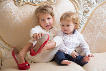 Girl and boy with blond hair sit on classic sofa