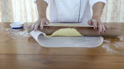 Wall Mural - Woman rolls dough on the table with a rolling pin.