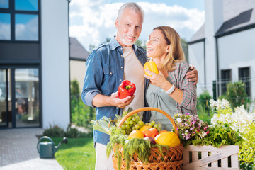 Nice peppers. Beaming happy couple feeling extremely satisfied after gathering peppers from their garden bed