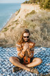 © Vaobullan - Cool guy in sweater and sunglasses playing ukulele on blanket near sea.