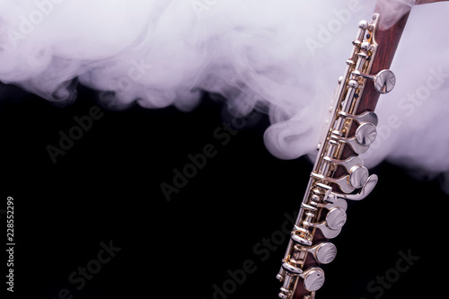 Fotografie, Obraz A piccolo flute from brown wood with silve plated keys in smoke on a black backg