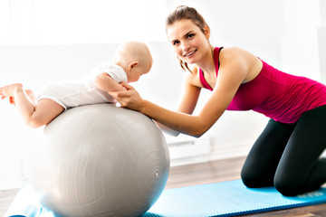 Wall Mural - A Portrait of beautiful young mother in sports wear with her charming little baby in training session