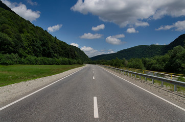 Empty asphalt road highway in the forested mountains, on the background a cloudy sky