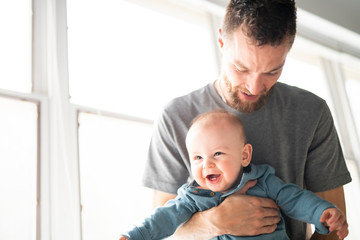 father holding his baby son in the arms close to a window