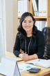 © DragonImages - Portrait of cheerful young financial manager sitting at office table with chart and planner on it