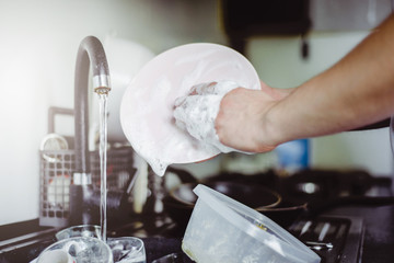 Wall Mural - The man washes the dirty dishes by hand with dish soap. Dirty dishes in the sink. No dishwasher. Concept of caring for dishes in the kitchen. The kitchen sink is full of dirty dishes.