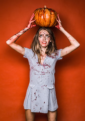 Wall Mural - Beautiful young surprised woman in costume holding pumpkin. Pretty young blonde woman clothed in dress with pumpkins. Vampire Witch lady with blood in mouth on red background.