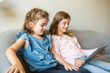 © Louis-Paul Photo - two sisters girls sit on the sofa at home with tablet