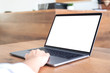 © Farknot Architect - Mockup image of hand using and typing at laptop with blank white desktop screen on wooden table in office