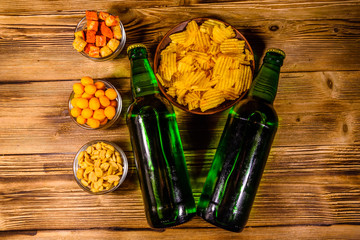 Two bottles of beer and different snacks on wooden table. Top view