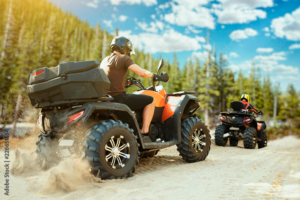 Two quad bike riders in helmets travels in forest - obrazy, fototapety, plakaty 