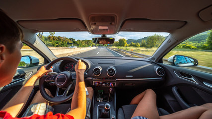 Wall Mural - Driver's hands on a steering wheel of a car and woman in the passenger seat. Road trip on the Italians road.