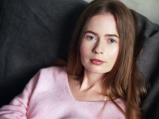 Natural light close up lifestyle portrait of beautiful blond woman with blue eyes long hair on sofa looking at camera