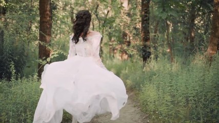 Poster - cute slender girl, dressed in a long white vintage transparent dress with floral patterns and a long waving train, runs along a narrow path in a forest. a boho style for runaway bride