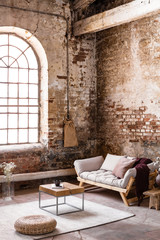 Wall Mural - Pouf and table on rug in front of beige settee in spacious loft interior with window. Real photo