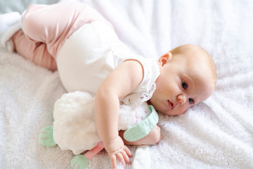 Adorable two months baby girl relaxing in bedroom on knitted blanket on a sunny morning