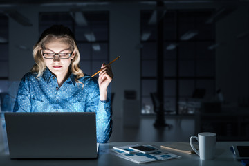 Beautiful blonde in dark office working on laptop and getting ne