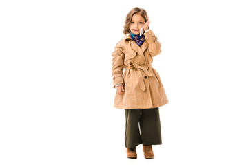 Wall Mural - beautiful little child in trench coat talking by phone and looking at cameraisolated on white