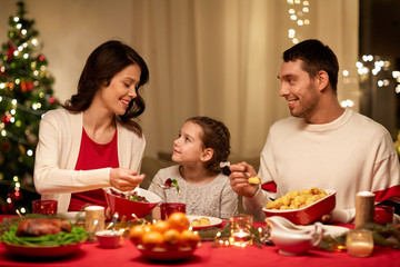 holidays, family and celebration concept - happy mother, father and little daughter having christmas dinner at home