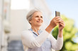 © Syda Productions - travel, tourism and technology concept - happy senior woman photographing by smartphone in city