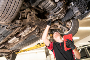 handsome mechanic based on car in auto repair shop with tablet on hand