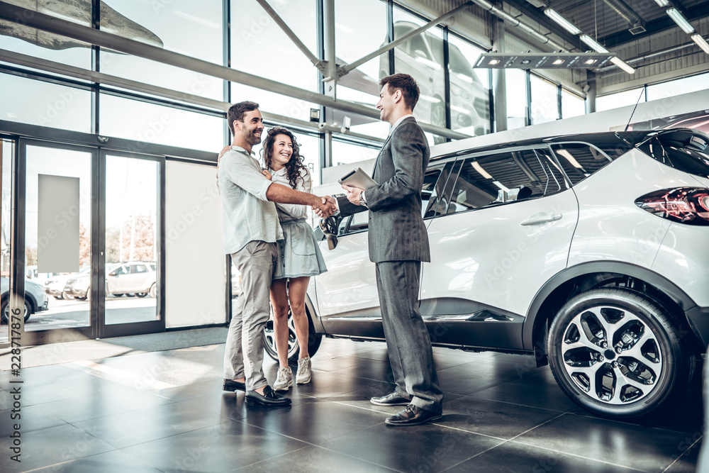 Young couple shaking hands with sales agent after a successful car buying - obrazy, fototapety, plakaty 